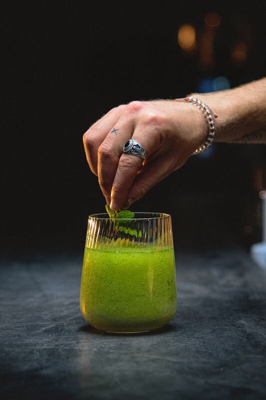 Bartender placing mint on a green cocktail